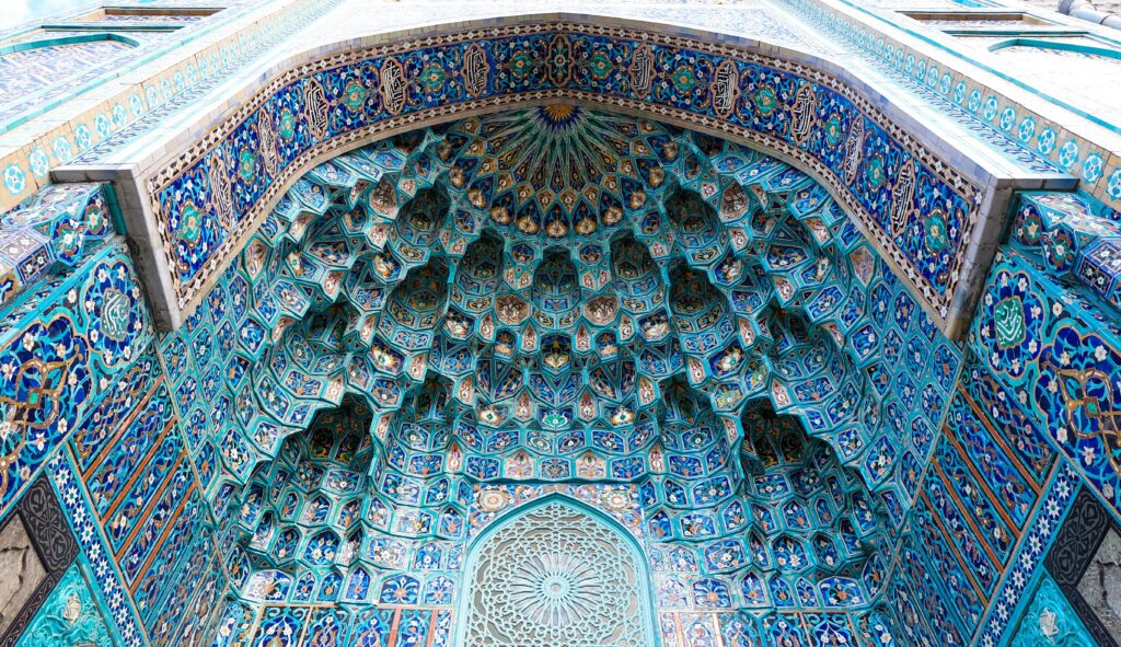A close-up view of an ornate Islamic dome with vibrant blue mosaic patterns and geometric design.