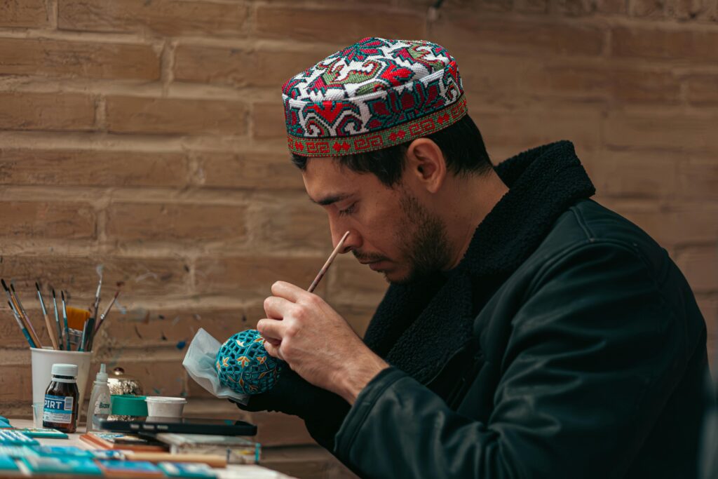 Uzbek artisan focuses on intricate traditional craft indoors, showcasing cultural artistry.