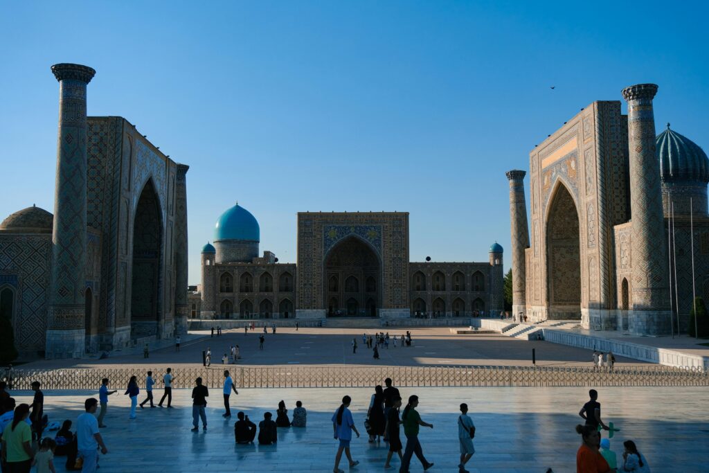 Crowded Registan Square in Samarkand with ancient madrasahs under a clear sky.